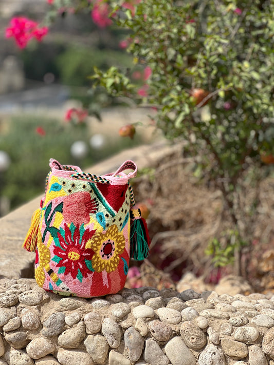 Colourful handwoven Wayuu tapestry handbag resting on stones near garden flowers