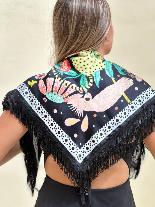 Back view of a woman wearing a black fringed scarf featuring intricate hand-illustrations