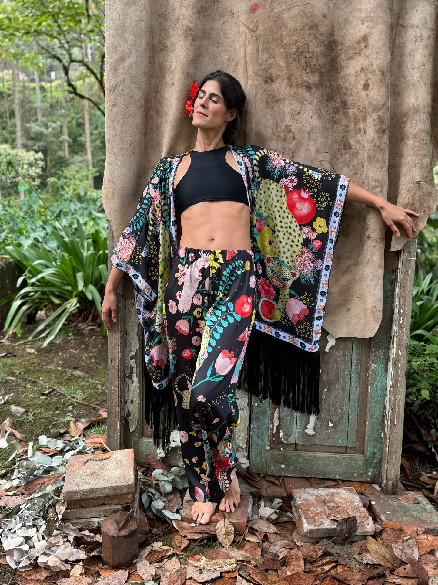 Full-body view of the Rita trousers styled with a black crop top and kimono, showing the vibrant illustrated pattern in an outdoor setting