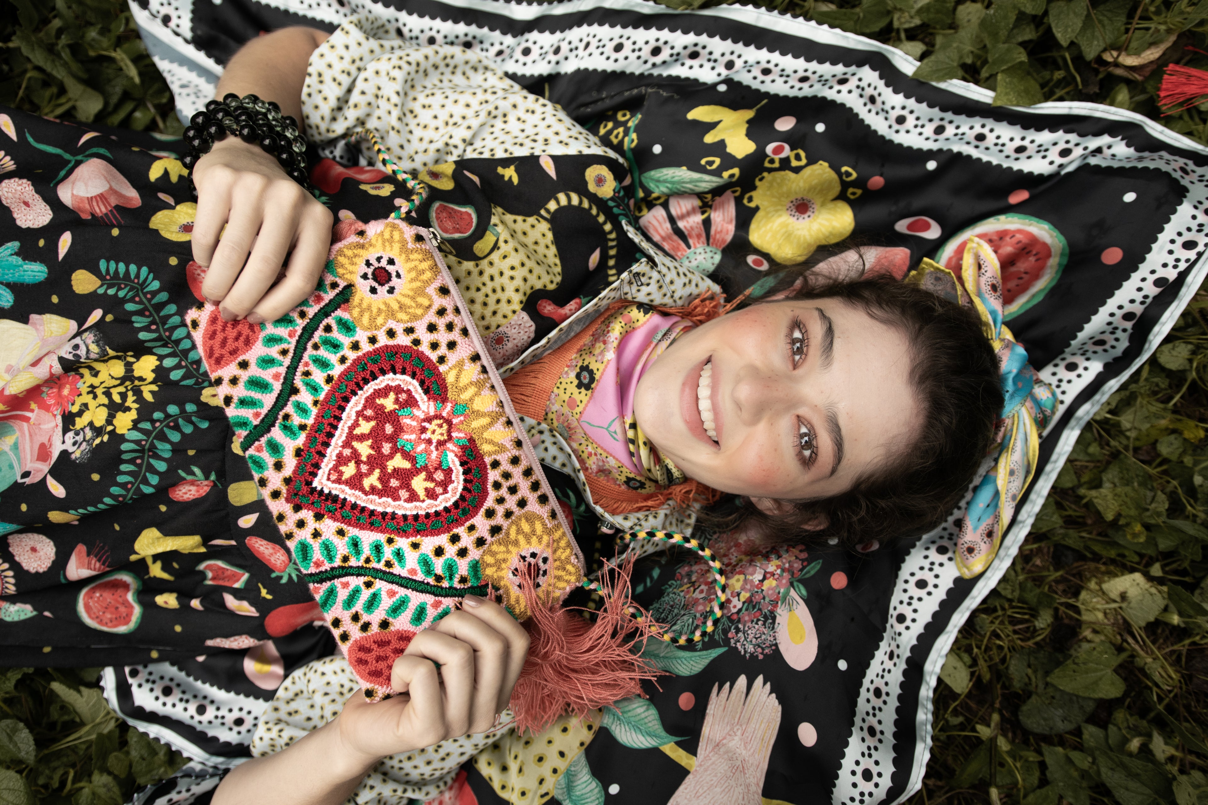 Model lying on black TelaCuento scarf holding the Heart Tapestry Clutch Bag, showcasing its handwoven details and vibrant Colombian colours.